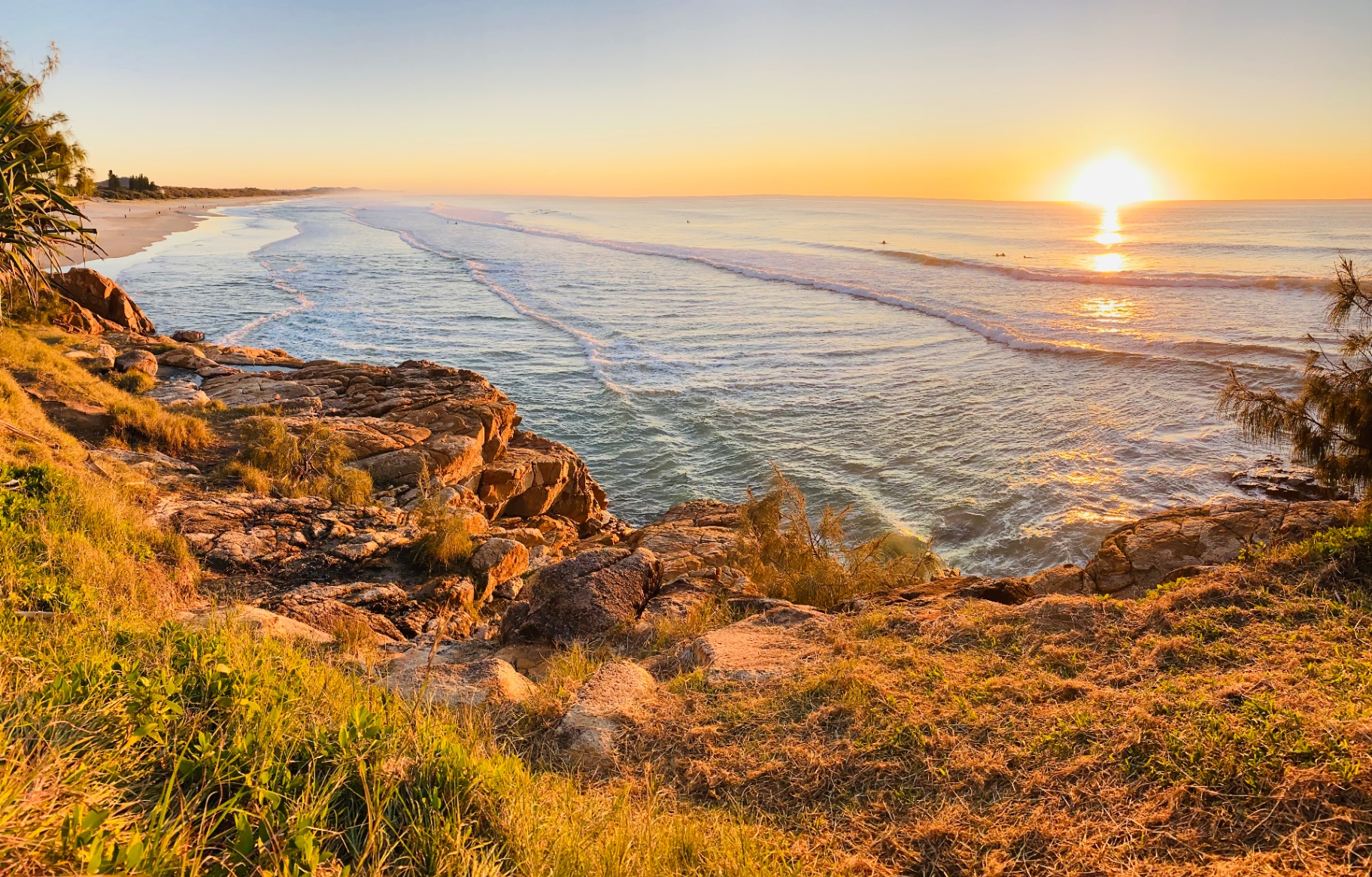 Sunrise over a Sunshine Coast beach with rocky headland and surf